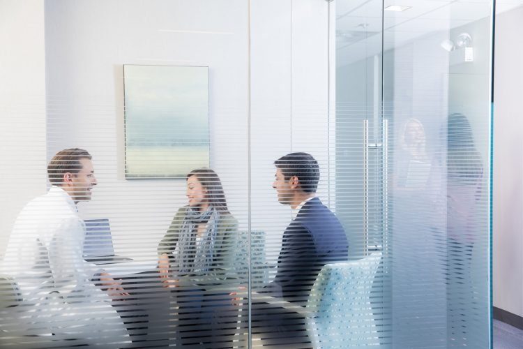 A professional consultation taking place behind a frosted glass partition, showing three people seated around a table in a bright, modern office.